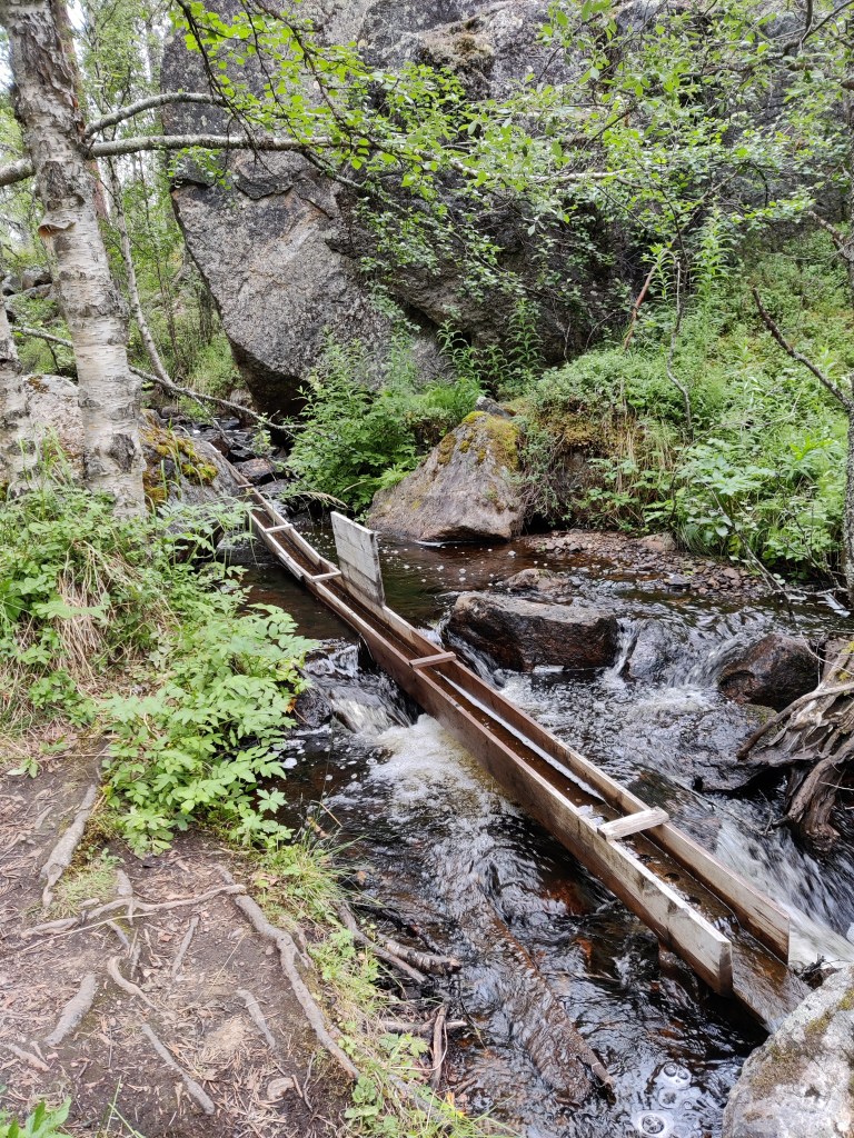 Kuva vuolaasti virtaavasta purosta, jossa on puinen kullanhuuhdonnassa käytetty  "kanava".