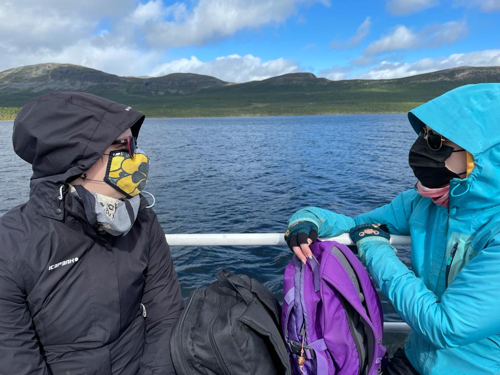 Kuva Katjasta ja Tainasta veneessä keskustelemassa. Kummallakin huput päässä ja maskit naamalla.