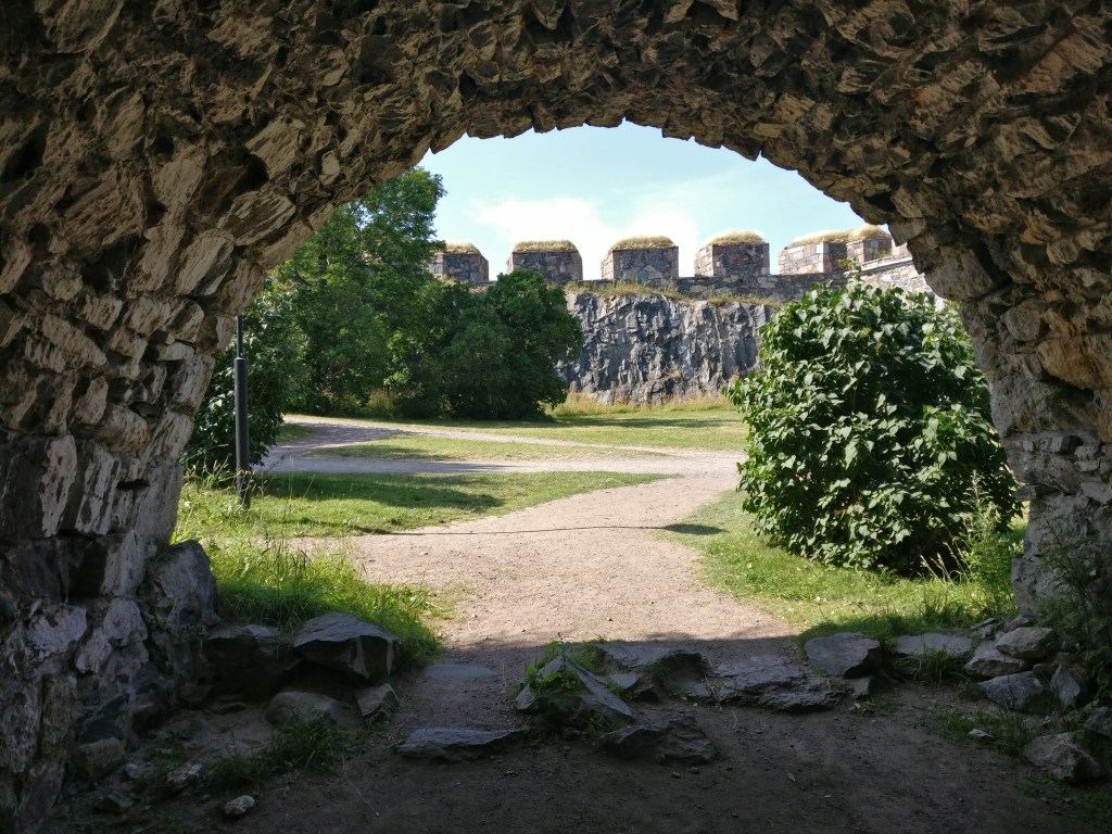 Kivisen, kaarevan muurin sisältä otettu kuva, jossa hiekkapolku mutkittelee eteenpäin. Taustalla kivestä rakennettu sakaraharjainen muuri.