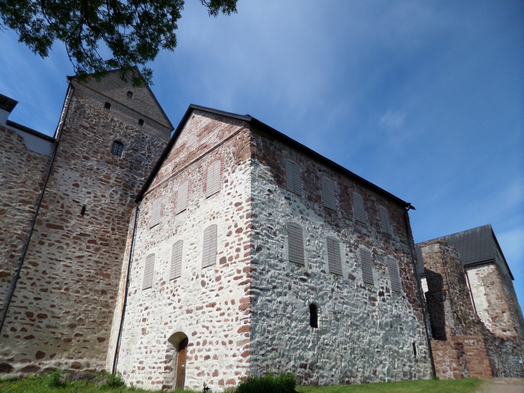 Kuva kivisen Kastelholman linnan juurelta. Linna on muodoltaan harjakattoinen ja "talon" kaltainen. Siinä on useita ikkunoita. Kiviaines on kulunut harmaaksi, osassa on vielä punertavaa väriä.