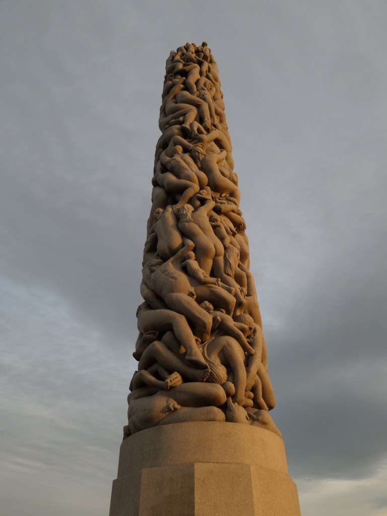 Kuva korkeasta, lieriönmallisesta veistoksesta, joka koostuu alastomista ihmisruumiista.