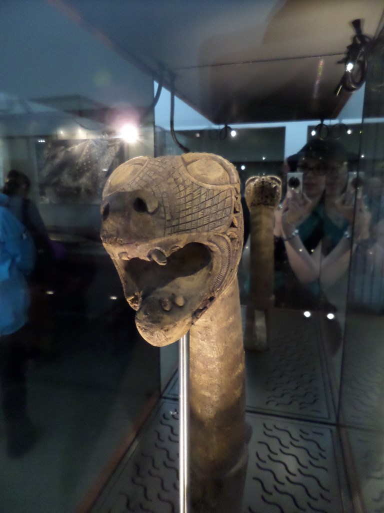 Vitriinin lasin läpi otettu erikoislähikuva puusta veistetystä eläinpäisestä laivan keulakuvasta.