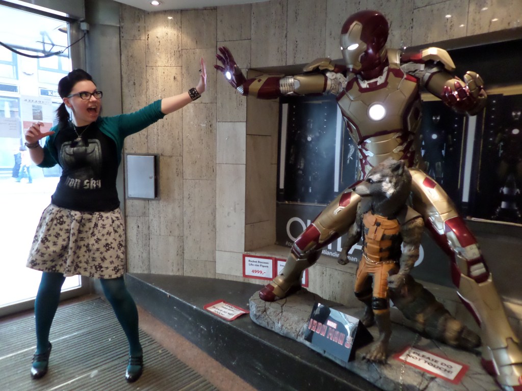 Kuvassa poseeraa Katja, jolla on päällä pääkallohame ja Iron Sky-t-paita. Hän ojentaa vasenta kättään kohti Iron Man -patsaan kohotettua oikeaa kättä. Iron Manin jaloissa on myös Rocket Raccoon pesukarhun patsas. Kyltit pyytävät, että ethän koske patsaisiin.