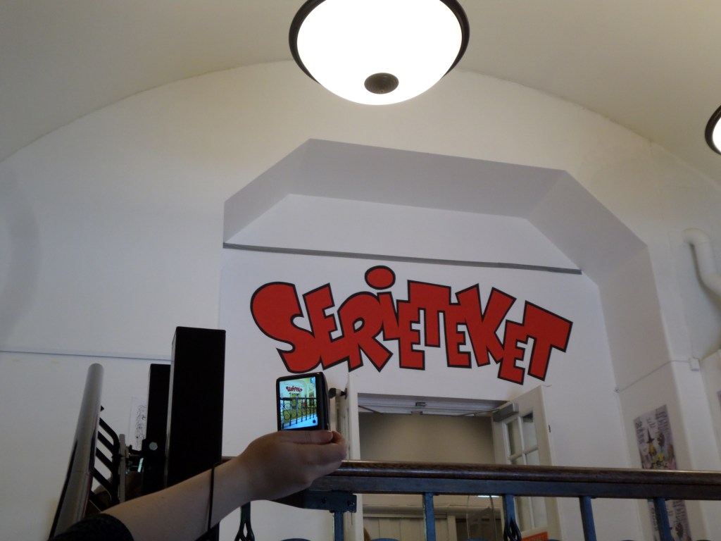 Kuva valkoisesta oviaukosta, jonka yläpuolella lukee punaisin, tyylitellyin kirjaimin SERIETEKET.