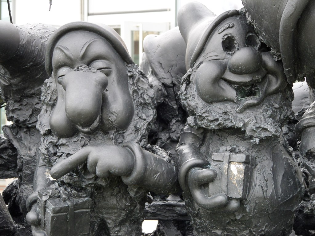 Erikoislähikuva veistoksesta ja kahdesta kääpiöstä (todennäköisesti Nuhanenä ja Lystikäs). Lystikkään silmät on kaiverrettu pois ja kummankin parrat ovat röpelöiset. Kummallakin on kädessään pieni lahjapaketti.