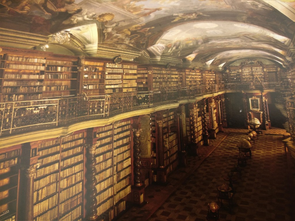 Kuva suuresta kirjastosalista, jonka seiniä kiertää kahden kerroksen verran vanhoja kirjoja. Lattia on kuvioitu ja sen keskellä on jonossa vanhoja maapalloja. Kattoon on maalattu enkeliaiheisia kuvia.