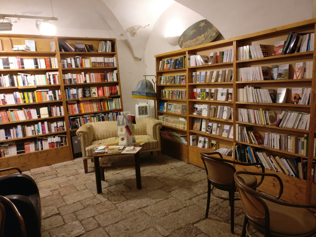 Kuva huoneen nurkasta, jonka kummallakin seinällä on useita kirjoja täynnä olevia hyllyjä. Näiden edessä on pieni sohva ja pöytä sekä lukulamppu. Etualalla on lisää tuoleja.