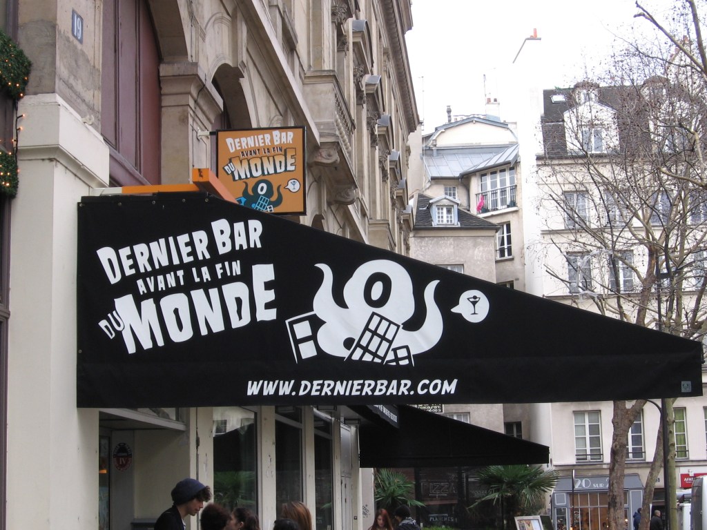Kuvassa musta markiisi, jossa lukrr Dernier Bar avant la fin du Monde. Logona on yksisilmäinen, tyylitelty mustekala, jonka puhekuplassa on drinkin kuva.