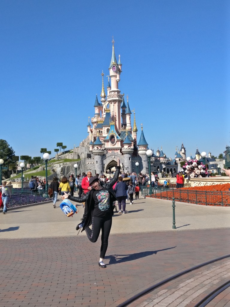 Kuva Katjasta heilumassa toinen jalka ilmassa ja Aku-reppu kädessä Prinsessa Ruususen linnan edessä.