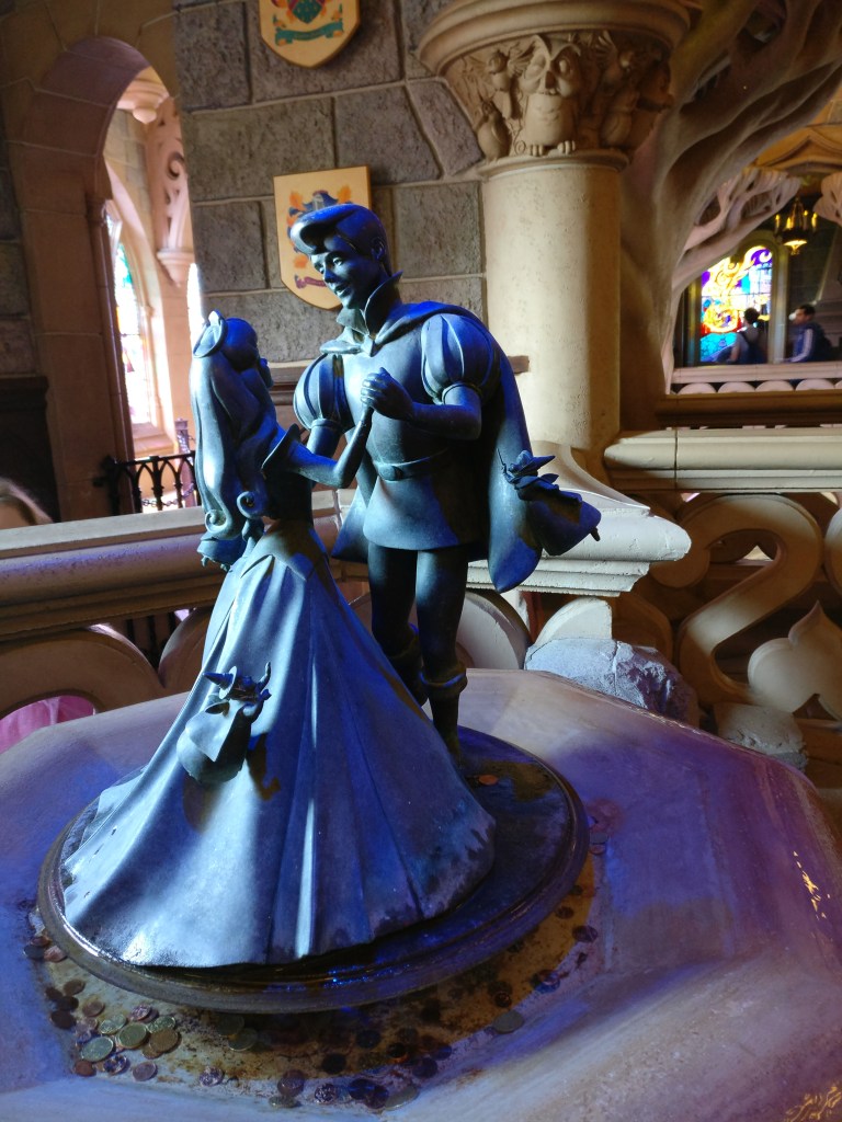 Erikoislähikuva pienestä patsaasta, jossa prinssi Philip tanssii prinsessa Ruususen kanssa. Heidän ympärillään pörrää myös kolme hyvää haltiakummia.