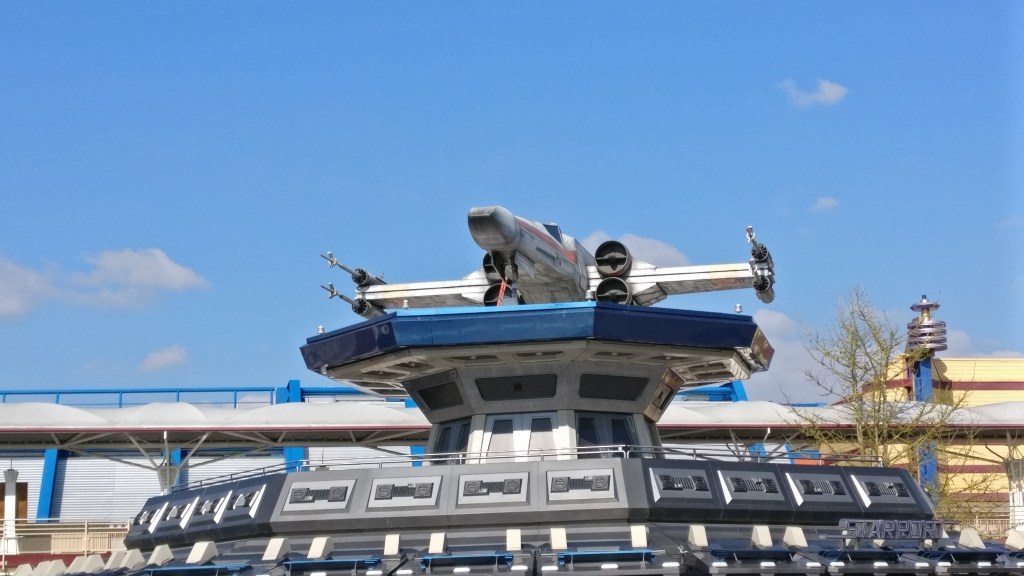 Kuvassa X-Wing-alus, joka on asetettu ison rakennuksen katolle.