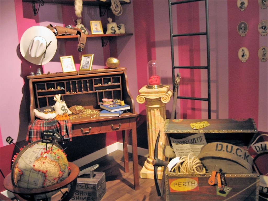 Kuvassa Roope Ankan elämä ja teot -kirjan pohjalta visualisoitu nurkkaus, jossa on erilaisia Roope Ankan muistoesineitä aina ensilantista matka-arkkuun ja maapalloon, johon on merkitty kaikki käydyt paikkakunnat.