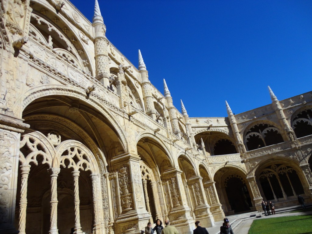 Kuva luostarin sisäpihalta, missä näkyy rakennuksen koristeellinen tyyli ja kauniit holvikaaret, jotka kehystävät käytävien suuaukkoja ja toisen kerroksen tasanteita.