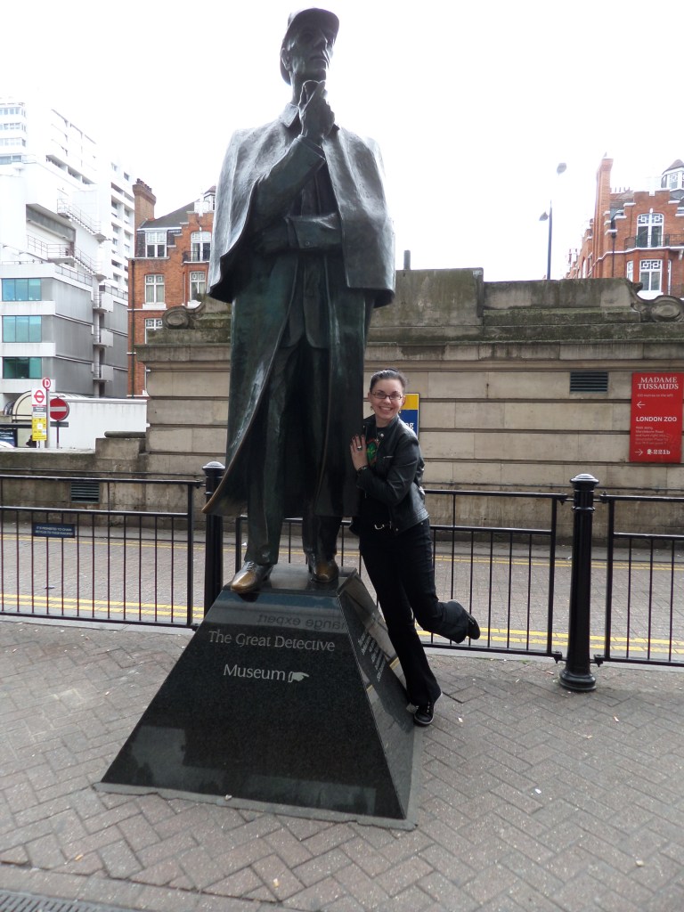 Kuva Katjasta, joka poseeraa hymyillen Sherlock Holmesin patsaaseen nojaten.