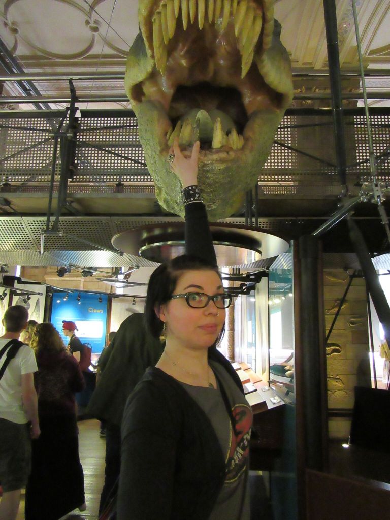 Kuva hieman nolosta Katjasta, joka on juuri ojentamassa kättään Tyrannosaurus rexin hampaita kohti.