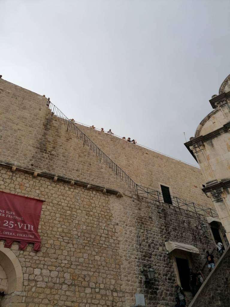 Kuva korkeasta, vaaleanruskeasta muurista, jonne vie kaiteella varustetut portaat. Muurin huipulla on ihmisiä, joista kolme reunimmaista ovat minä ja siskoni, mutta meitä ei voi erottaa tai tunnistaa kuvan perusteella.