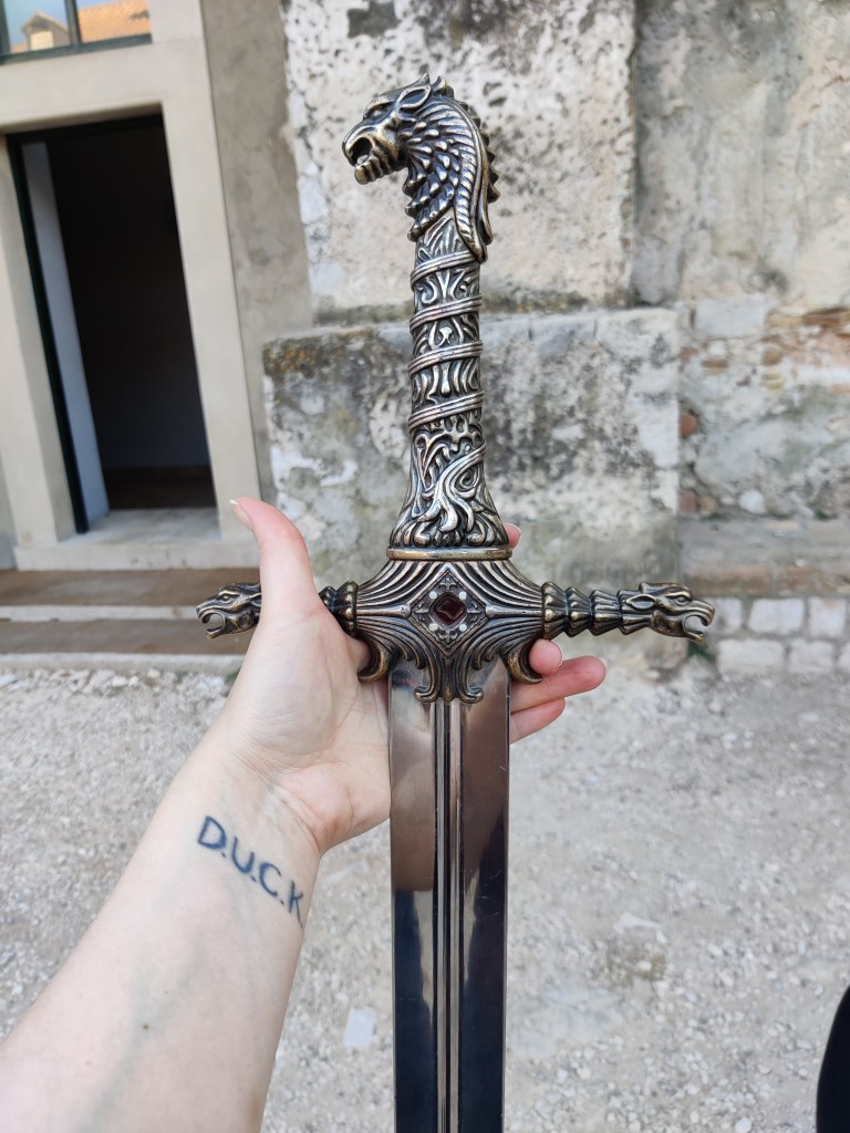 Erikoislähikuva miekasta, jonka kahva on koristeellinen ja ponnessa on leijonanpää.