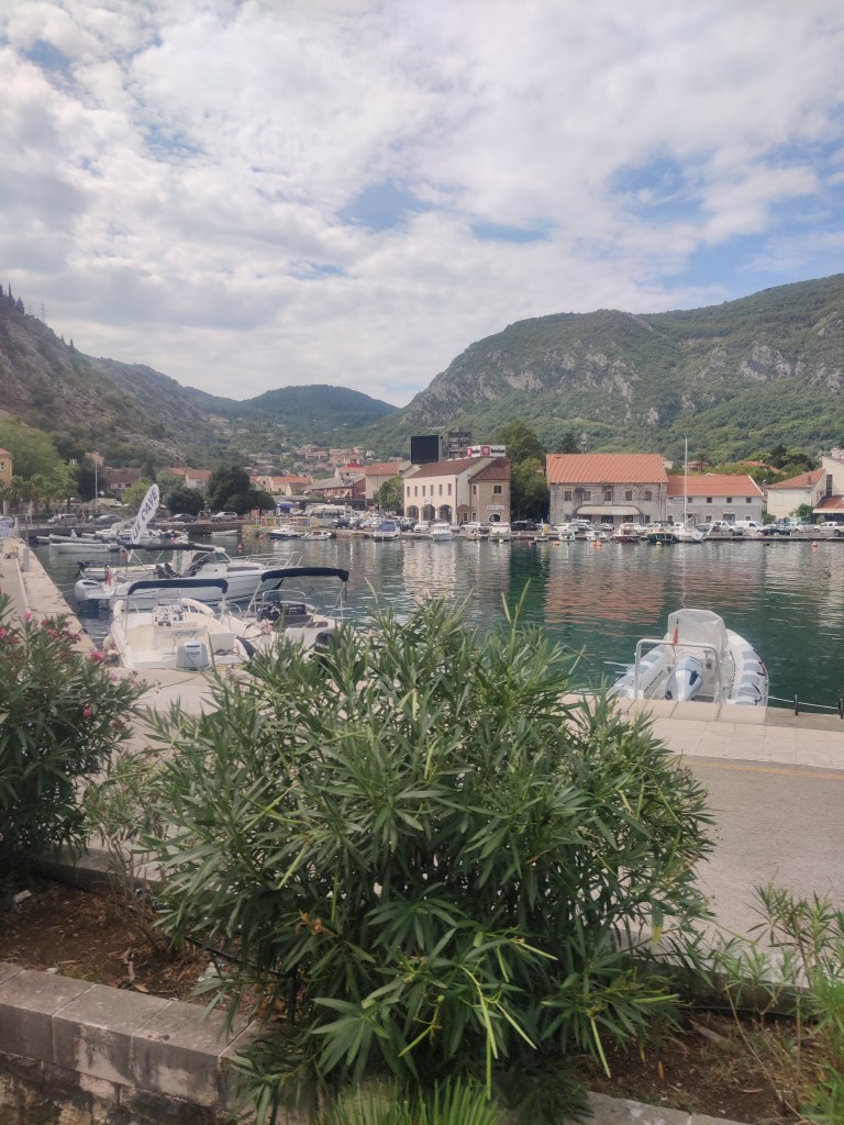 Kuvassa lahdenpohjukassa oleva satama. Etualalla pari puskaa, joiden takana erottuu pieniä moottoriveneitä, joita näkyy myös lahden toisella puolella. Oranssitiilikattoiset talot reunustavat lahtea. Niiden takana on kasvillisuuden peitossa olevaa vuoristoa.