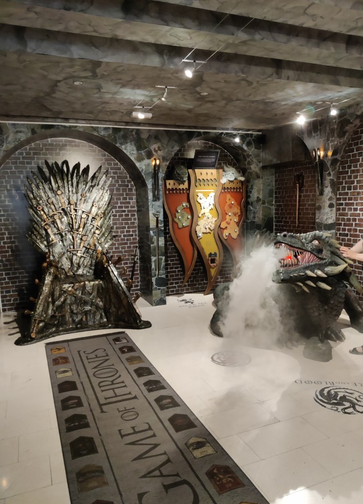 Kuva House of Game -kaupan sisätiloista, jossa on muun muassa muovinen rautavaltaistuin, erilaisia pelejä ja lohikäärme, jonka suusta pihisee savua.