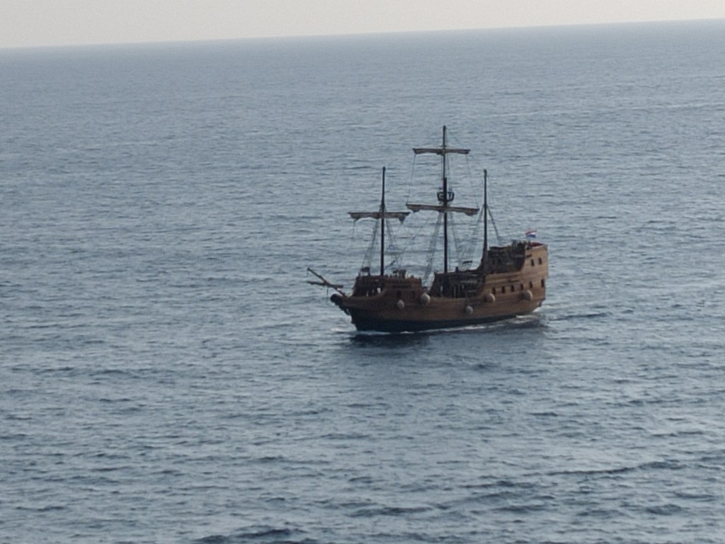 Kuva merellä seilaavasta vanhasta, ruskeanvärisestä purjelaivasta, jonka purjeet on nostettu ylös.