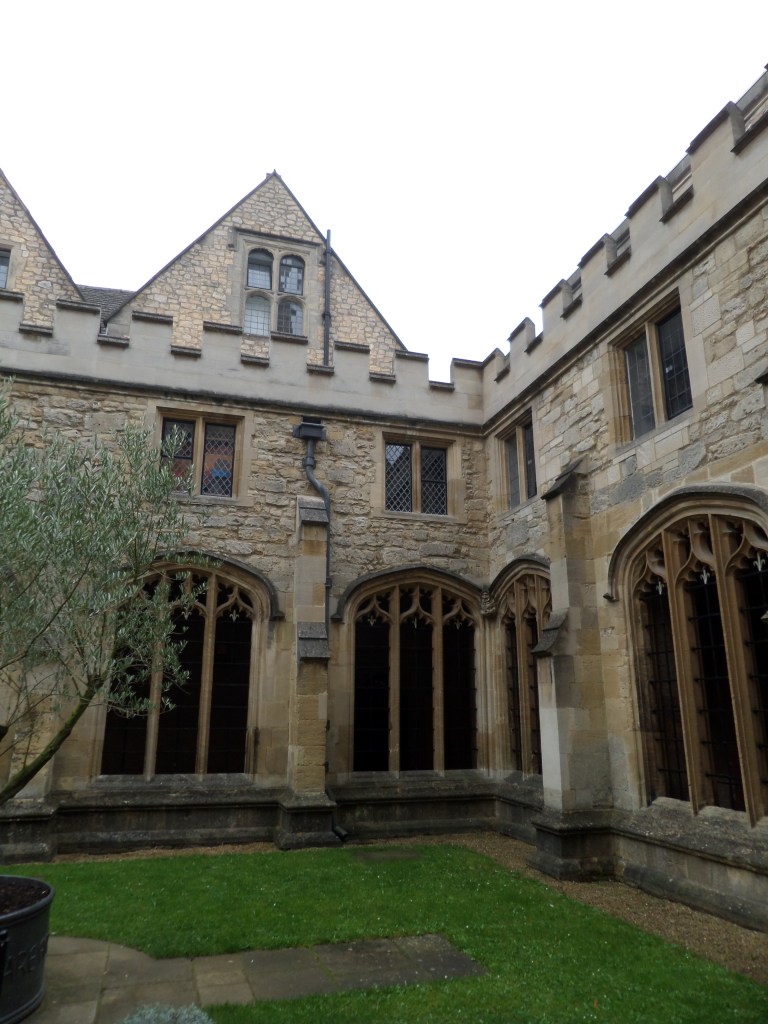 Tiivis maisemakuva Christ Churct -collegen sisäpihalta, jossa näkyy nurmikko, puu ja rakennuksen pyöreät, koristellut holvikaaret, joiden alla voi kävellä.