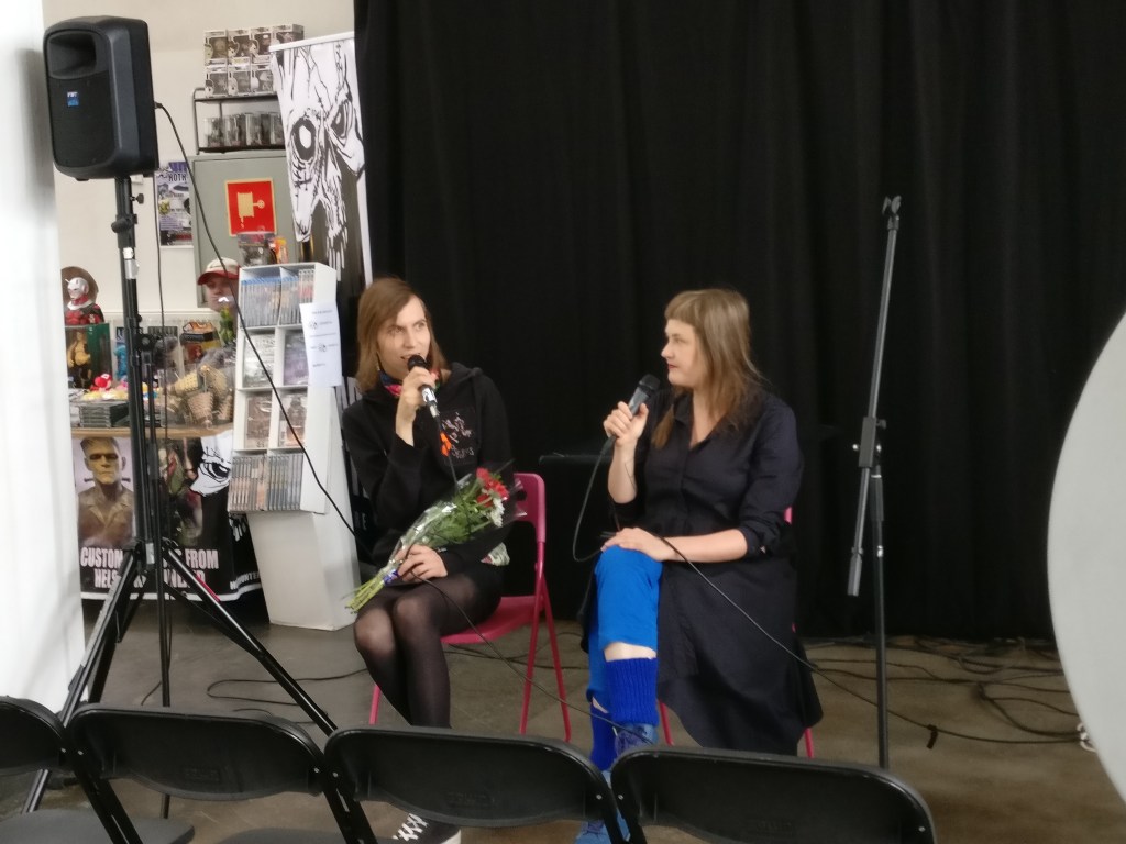 Sarjainfon päätoimittaja Aino Sutinen haastattelee blogipalkinnon voittanutta Jiipu Uusitaloa, joka pitelee sylissään kukkakimppua.