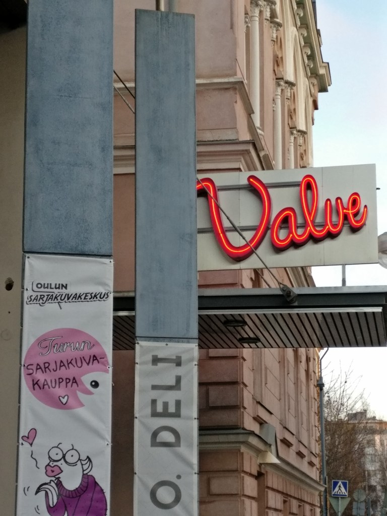 Oulun kulttuuritalo Valveen valokyltti ja Oulun sarjakuvakeskuksen banderolli, jossa myös Turun sarjakuvakaupan mainos.
