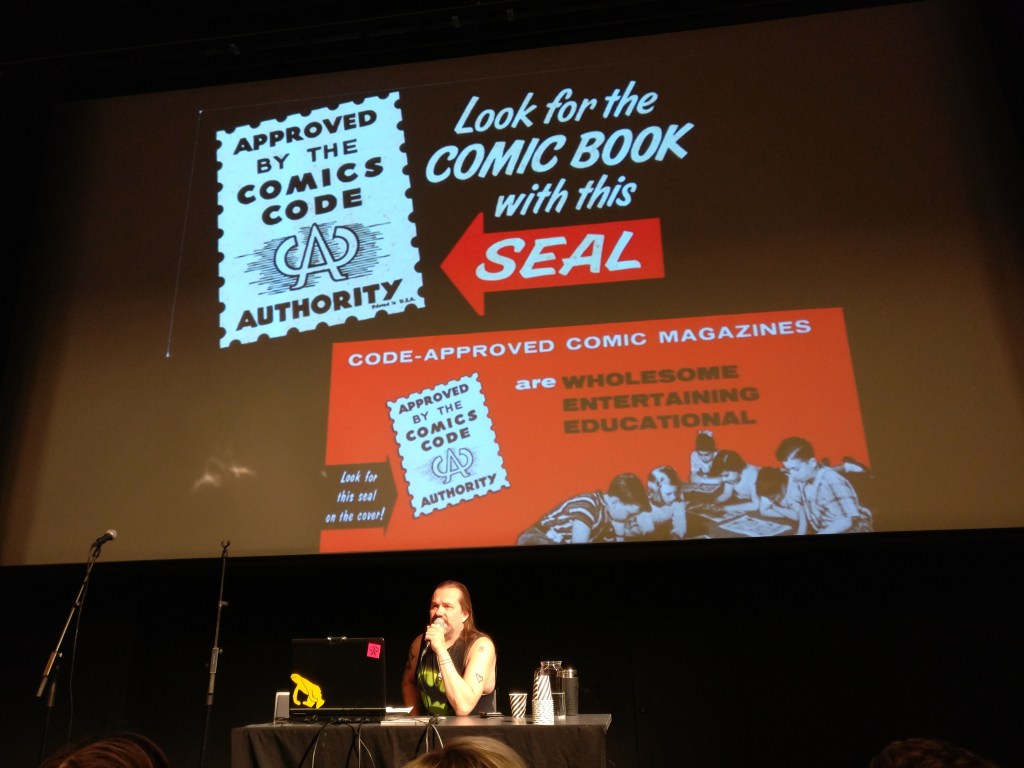 Petri Hiltunen pitää esitelmää sarjakuvasensuurista. Taustalla diat Comics Code -sinetistä.