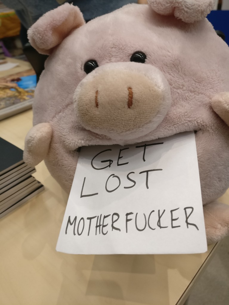 Pehmolelupossu, jonka suussa on lappu, jossa lukee GET LOST MOTHERFUCKER.