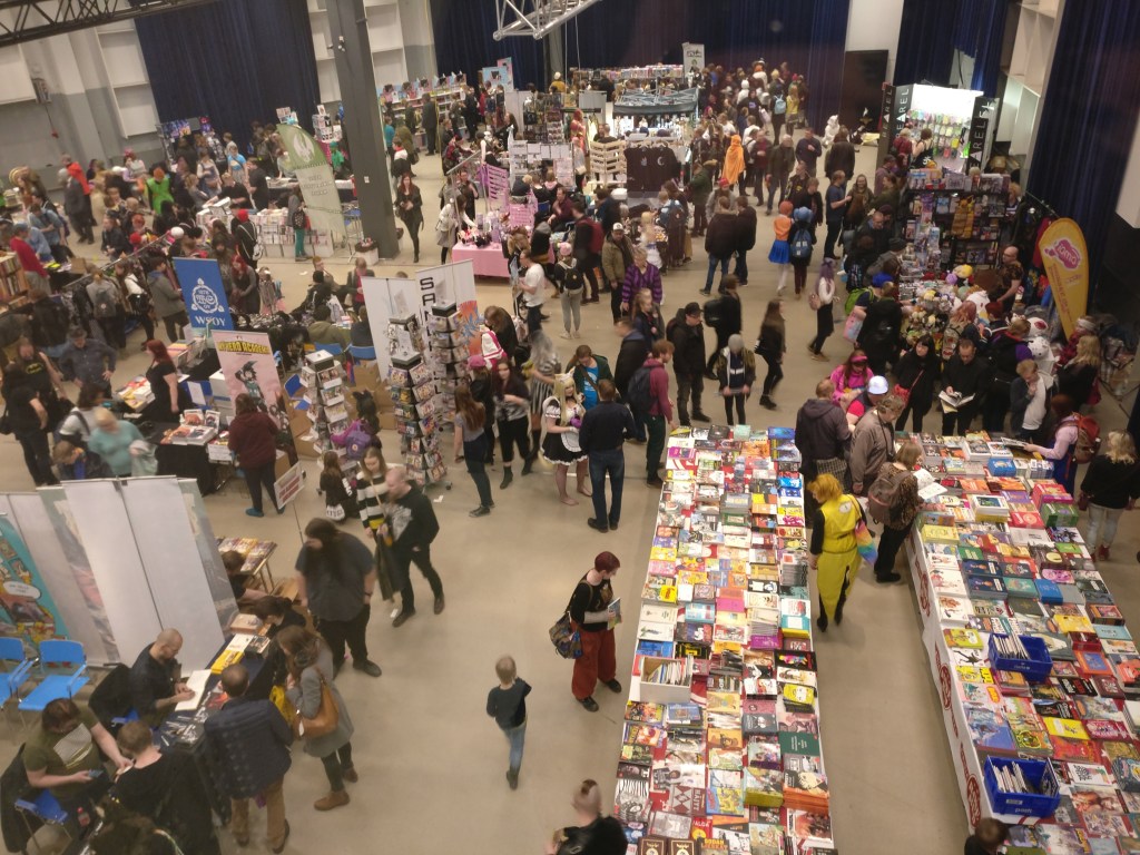 Ylhäältä otettu kuva Tampere-talon Sorsapuistosalista, joka on täynnä sarjakuvamyyntipöytiä ja ihmisiä.