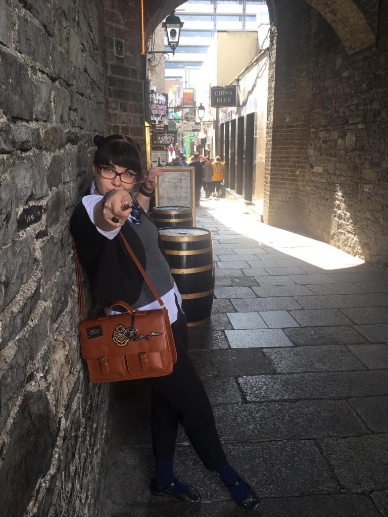 Kokokuva: Katja osoittaa kameraa taikasauvalla yllään Potter-teemaiset vaatteet. Kuva on otettu kapealla vanhalla ostoskujalla.