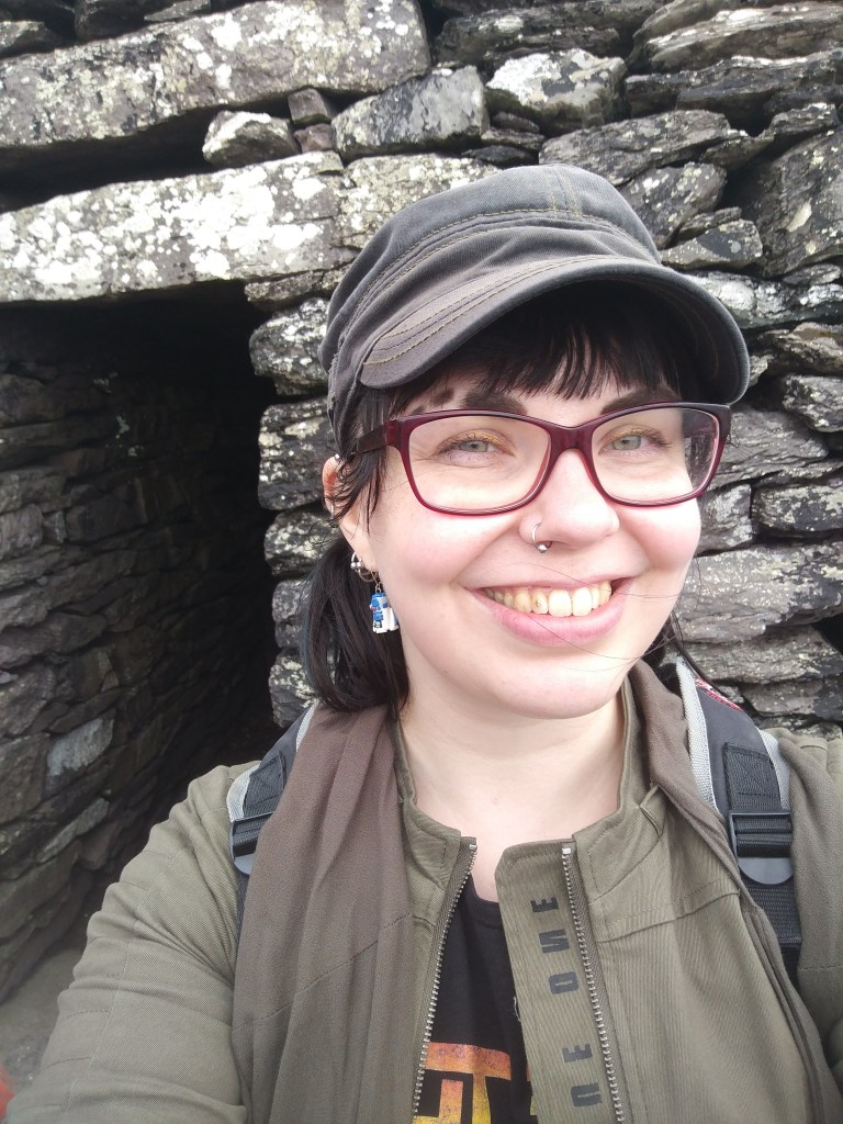 Selfie Katjasta hymyilevässä leveästi kivisen majan sisäänkäynnin edustalla.