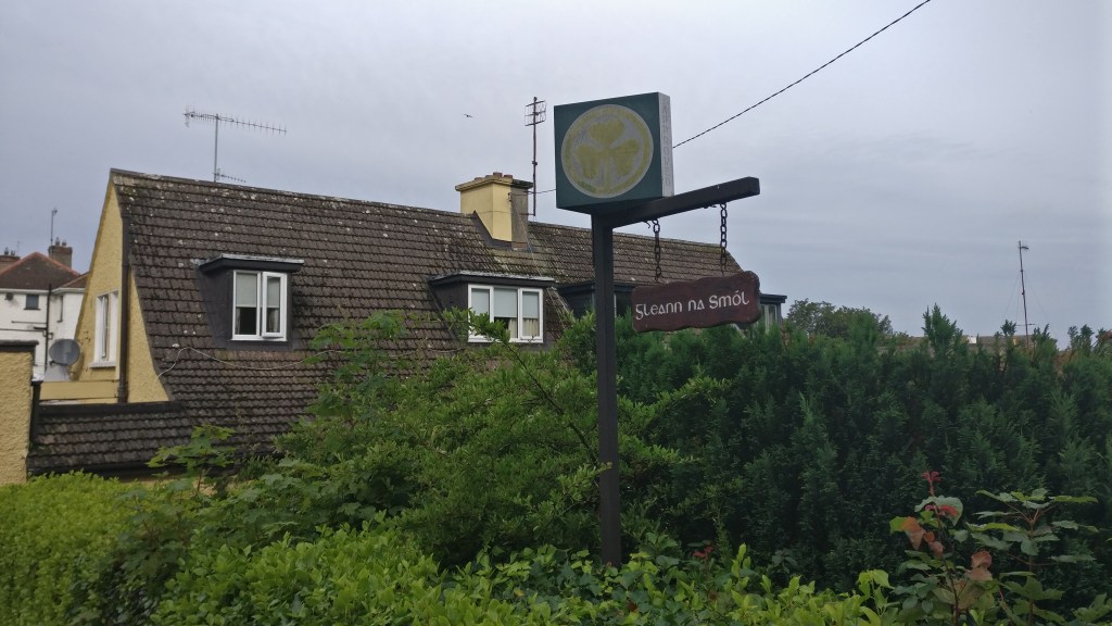 Kuvassa pensasaiden takana isohko tiilikattoinen omakotitalo, etualalla kyltti, jossa lukee majoituspaikan nimi.