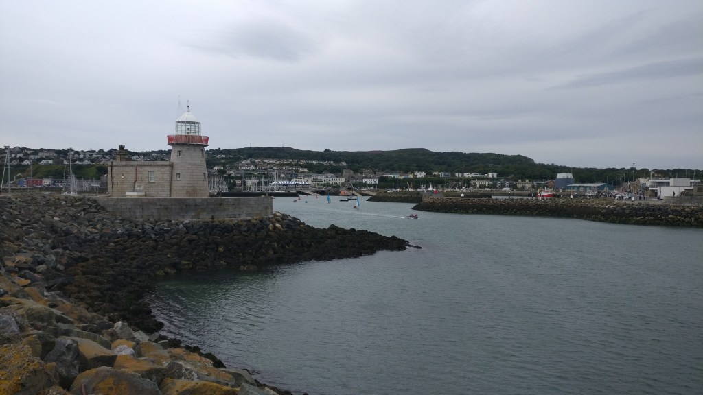 Kuva satamasta, jossa kivikkoisella aallonmurtajalla seisoo pieni majakka. Taustalla rannalla itse kylä.