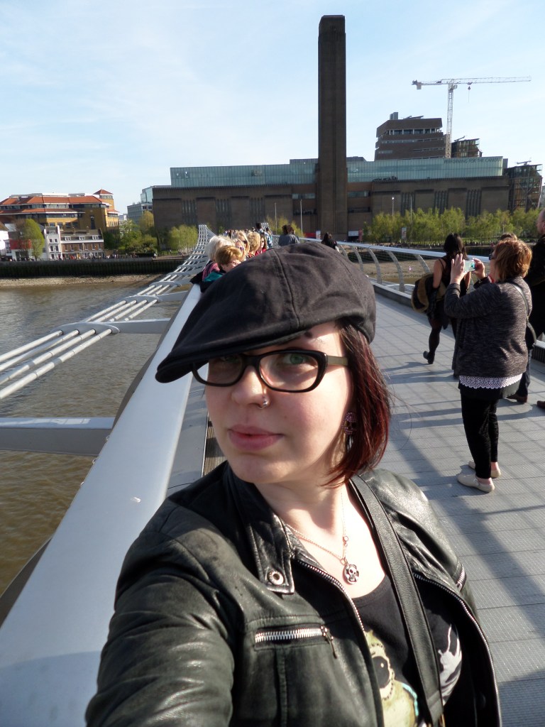 Katjan selfie Lontoon Millennium-kävelysillalla. Päällä musta nahkatakki ja päässä musta lätsä.