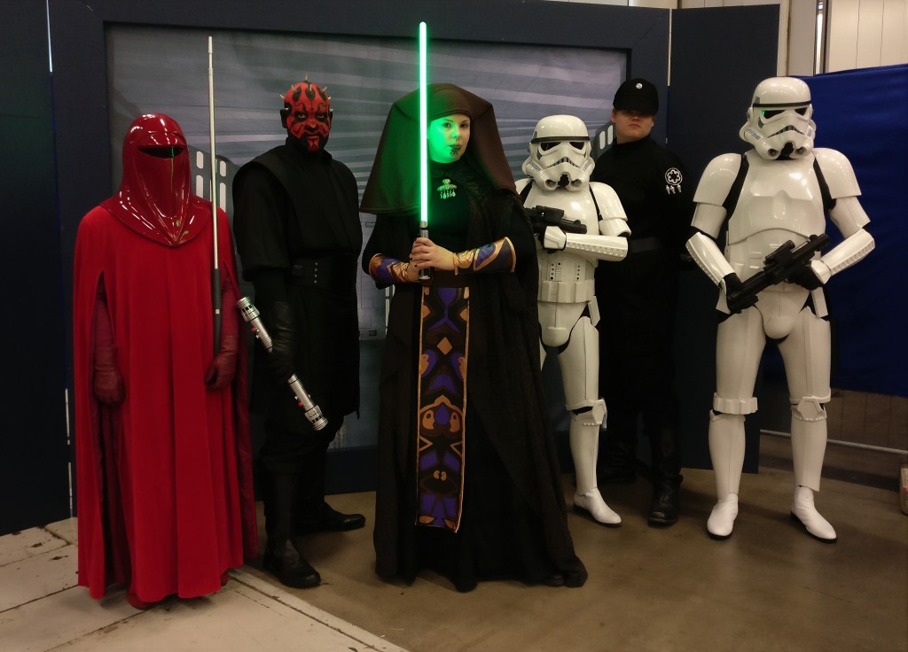 Ryhmäkuva porukasta, jossa on punaiseen kaapuun ja kypärään pukeutunut keisari Palpatinen henkivartiokaartilainen, mustissaan oleva Darth Maul, jonka naama on tatuoitu punamustin kuvioin, Luminara Unduli ruskeassa päähineessä ja mustassa kaavussa vihreän valomiekan kanssa. Lisäksi mukana kaksi valkoisessa haarniskassa olevaa Stormtrooperia ja yksi mustassa uniformussa oleva imperiumin upseeri.