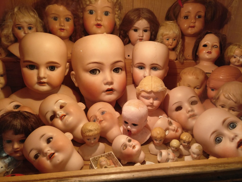 Kuva hyllystä, jossa on kasa nukenpäitä. Valtaosa on hiuksettomia, osalta puuttuvat silmät.