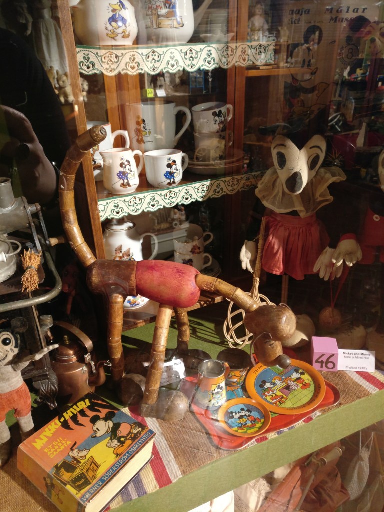 Kuvassa näyttelyhylly, jossa esillä vanhoja Mikki Hiiri -leluja sekä Disney-astiastoja.