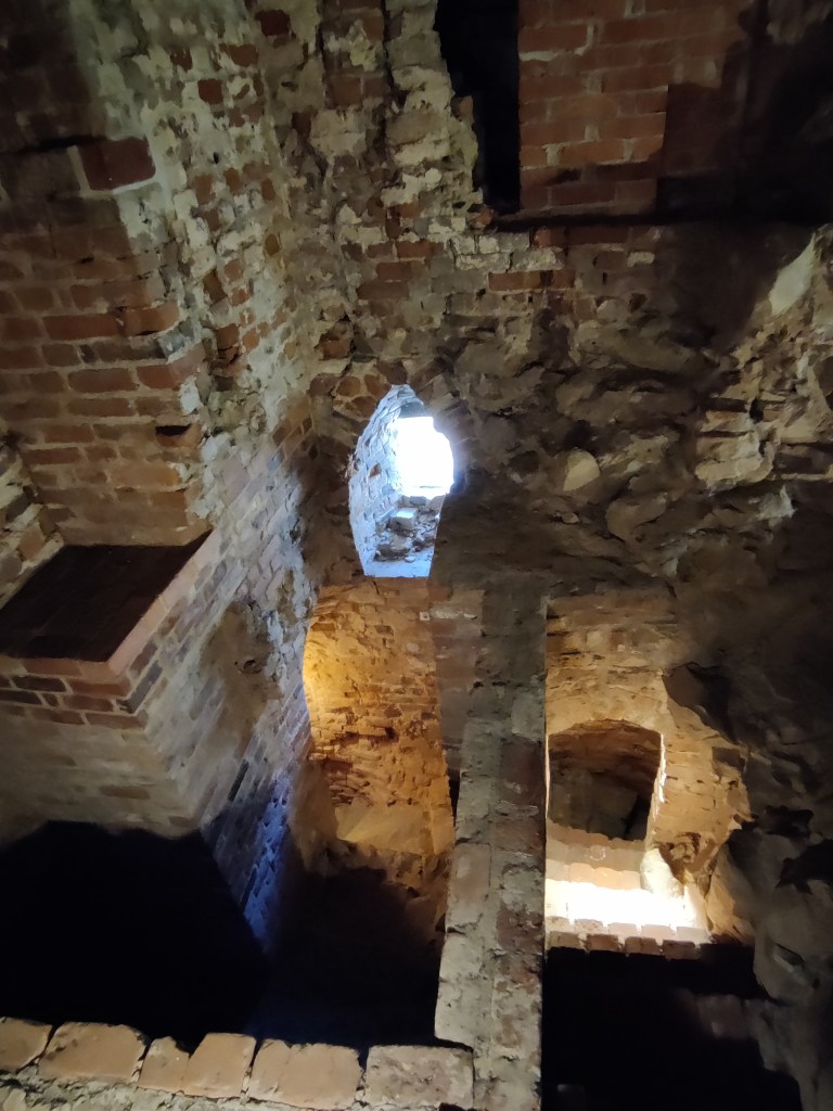 Kuva tiilistä ja kivestä rakennetusta, rapistuneesta huoneesta, jossa suoraan alapuolella kahdet eri portaat, joita erottaa muuri. Vastakkaisella seinällä kapea ikkuna muurissa.