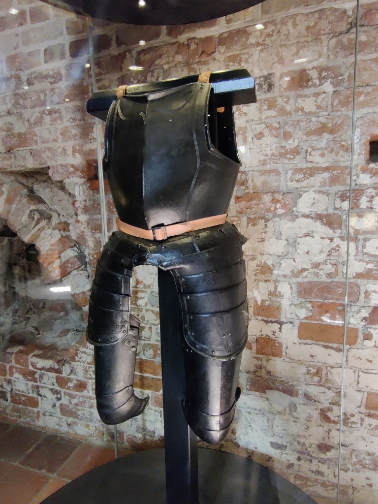 Kuvassa yksinkertainen, tumma, lähes musta haarniskan yläosa, jossa rintapanssari ja reisien sivussa suojaavat levyt.