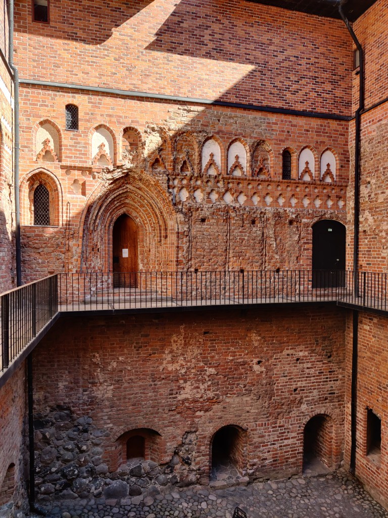 Kuva linnan sisältä, sisäpihan punatiilisistä seinämuureista.  Toisessa kerroksessa kulkee parveke, joka kiertää seinustaa. Toisen kerroksen oviaukon ympärillä näkyvä koristeelliset tiilikuviot.