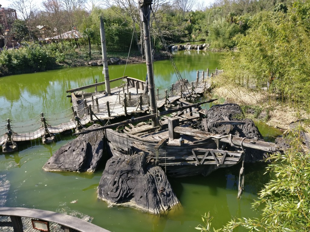 Kuva puisesta purjelaivasta, joka on kuin haaksirikkoutunut isojen kivien väliin. Laitan läpi kulkee kävelysilta.