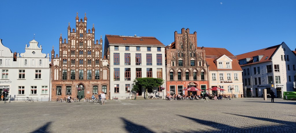 Torin reunalla rivi korkeita taloja, joista suuri osa on vaaleita, mutta kaksi on punaista tiiltä. Niissä on koristeelliset ikkunapuitteet ja julkisivut, joissa on pieniä tornimaisia ulokkeita.