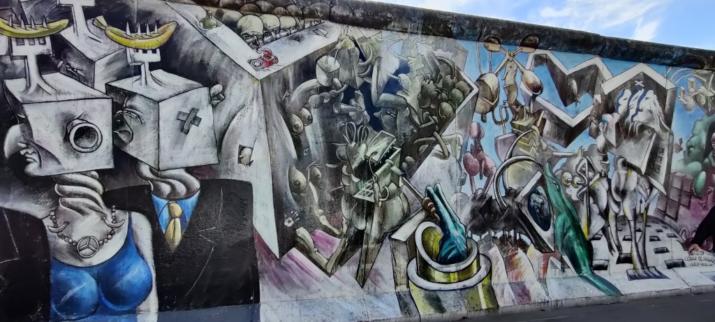 Pätkä abstraktia katutaidetta, josta erottuu parhaiten vasemmalla etualalla olevat naisen ja miehen hahmot. Heidät on kuvattu torsoista ylöspäin: naisella on sininen, rintoja korostava mekko ja mersun logolla varustettu kaulakoru, miehellä puku ja keltainen solmio. Heidän kuution malliset päänsä ovat kääntyneet vasemmalle.