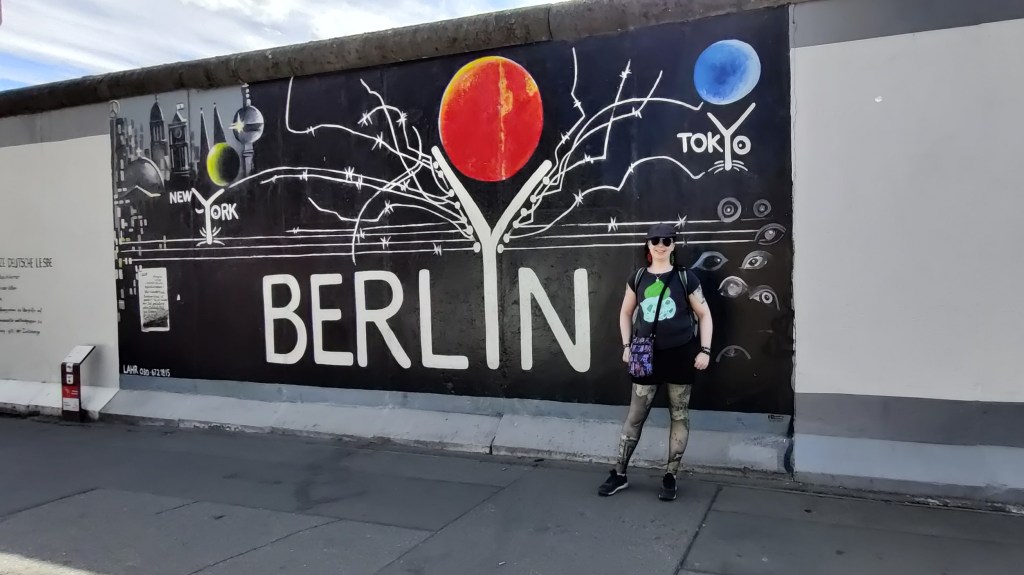 Kuva Katjasta, joka seisoo muurin edessä aurinkolaseissaan ja Bulbasaur-t-paidassa. Taustalla on musta maalaus, jossa lukee valkoisella BERLIN sekä pienemmällä fontilla NEW YORK ja TOKYO. Berlin-sanan I näyttää Y-kirjaimelta ja jokaisen Y:n päällä on erivärinen pallo, kuin planeetta. Kuvan vasemmassa seurassa on kaupunkimaisemaa, mm. Berliinin televisiotorni. Maalauksen keskellä kulkee kolme valkoista viivaa kuin piikkilankaa.