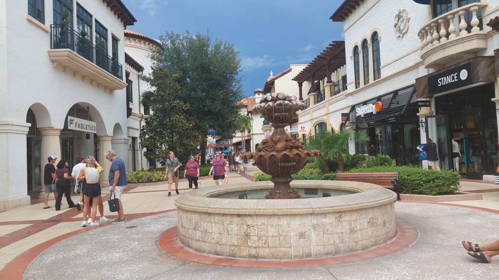 Kuvassa kivetty ostoskatu, jonka kummallakin puolella oli valkeaksi kalkittuja tiilirakennuksia, joissa oli pieniä, ranskalaisia parvekkeita. Keskellä katua on pensasistutuksia ja puita. Kuvan keskustaa hallitsee tummanruskea suihkulähde.