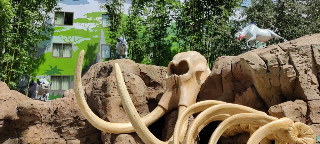 Leinonakuningas-elokuvasta otetusta kohtauksesta rakennettu kuvaelma, jossa kolme hyeenaa seisovat kallion päällä ja tuijottavat alas. Valtava norsun luuranko nojaa kallioon.