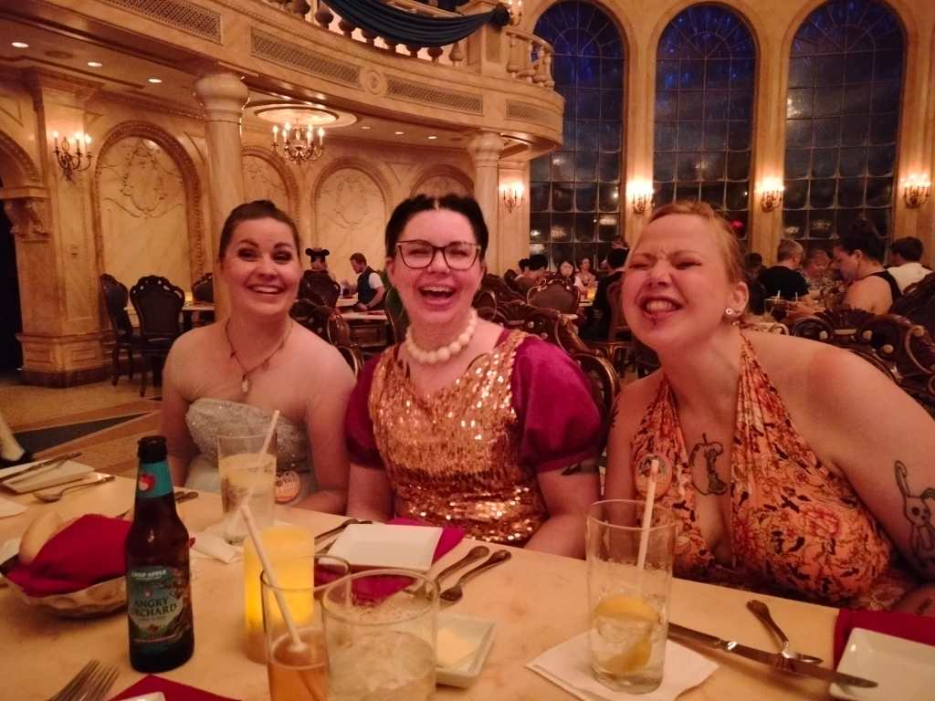 Kuvassa Tarja, Katja ja Hanna, joista kaksi ensimmäistä hymyilee ja kolmas irvistää ruokaa odotellessa. Taustalla näkyy upea, iso tanssisali, joka toimii ravintolana.