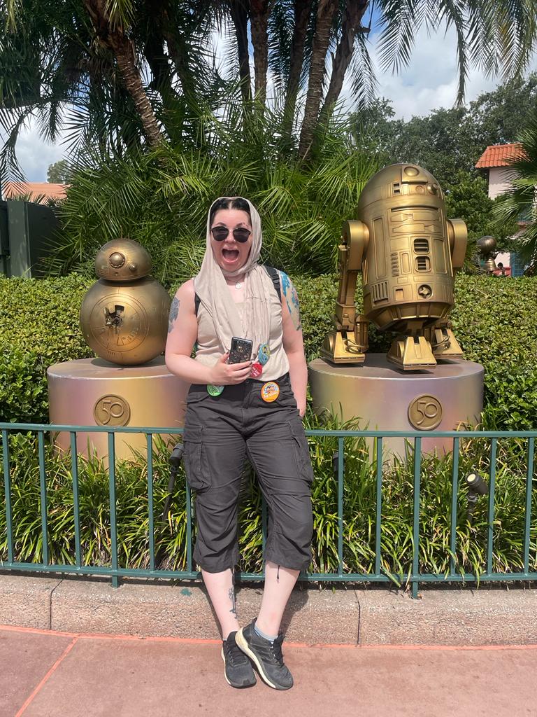 Kuvassa Katja poseeraa Star Wars -elokuvista tuttujen BB8- ja R2-D2 -droidien patsaiden edessä. Katjalla on aurinkolasit, päässä huivi ja vaatetyyli on muuten maanläheinen. Suu on auki innostuksesta ja toisessa kädessä on kännykkä.