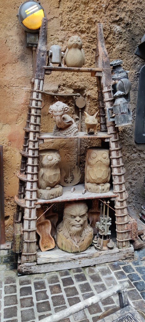 Kuvassa hyllykkö, jossa on useita erilaisia puusta kaiverrettuja patsaita: alarivillä näyttää olevan wookieen pää, keskitasolla kaksi porgia ja jedien logo, ylätasolla ithorialaisen pää sekä pieni loth-kissa.